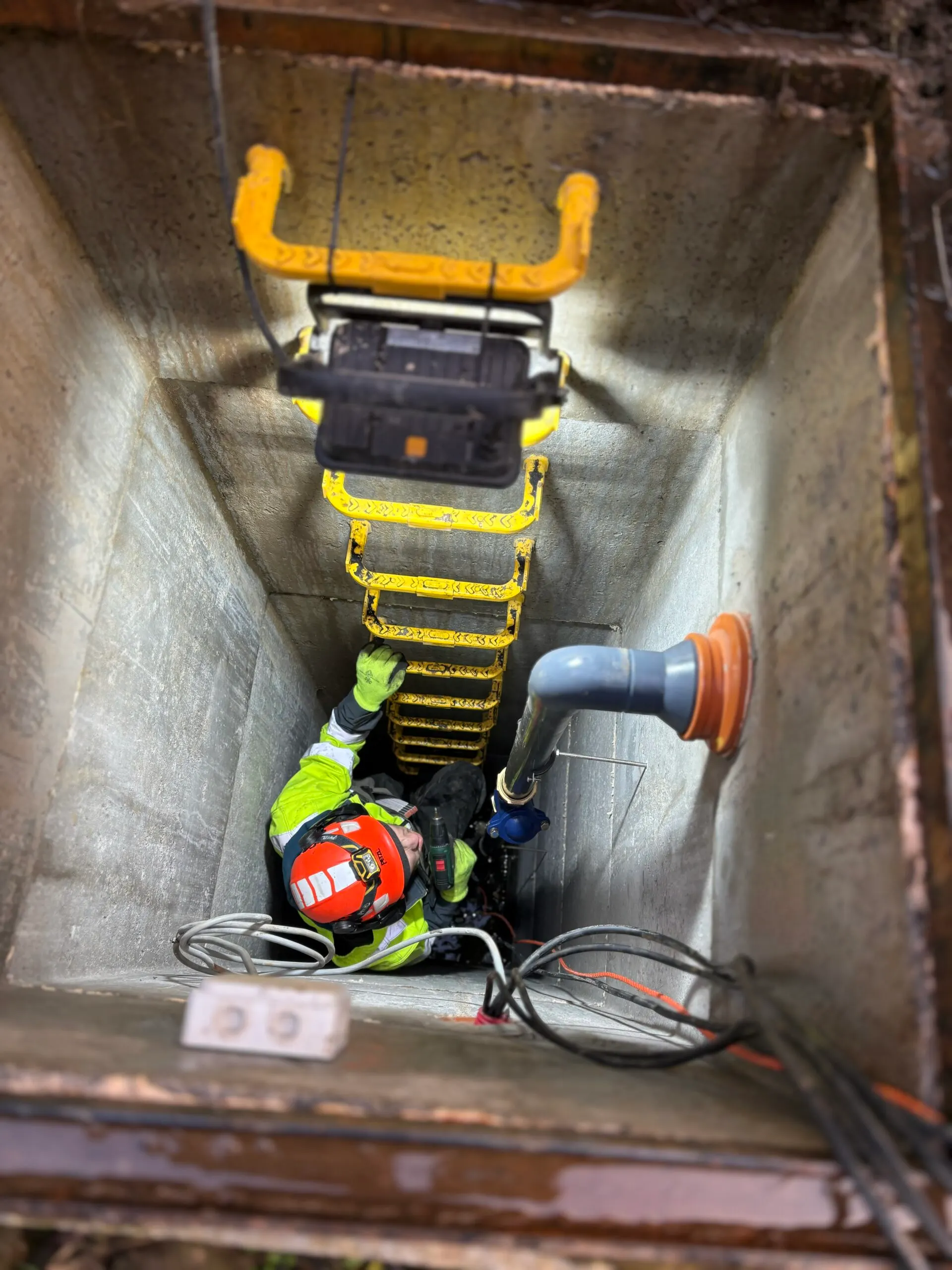 Technicus met helm en harnas aan het werk in een betonnen inspectieput