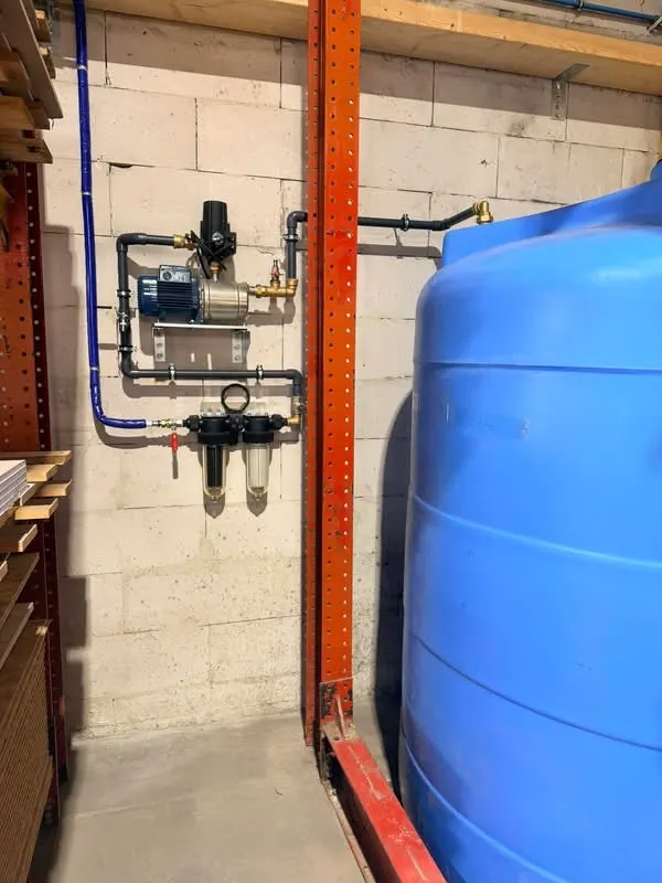 Cuve de stockage d’eau de pluie bleue à côté d’un groupe de pompage mural et de deux filtres, dans un atelier de menuiserie